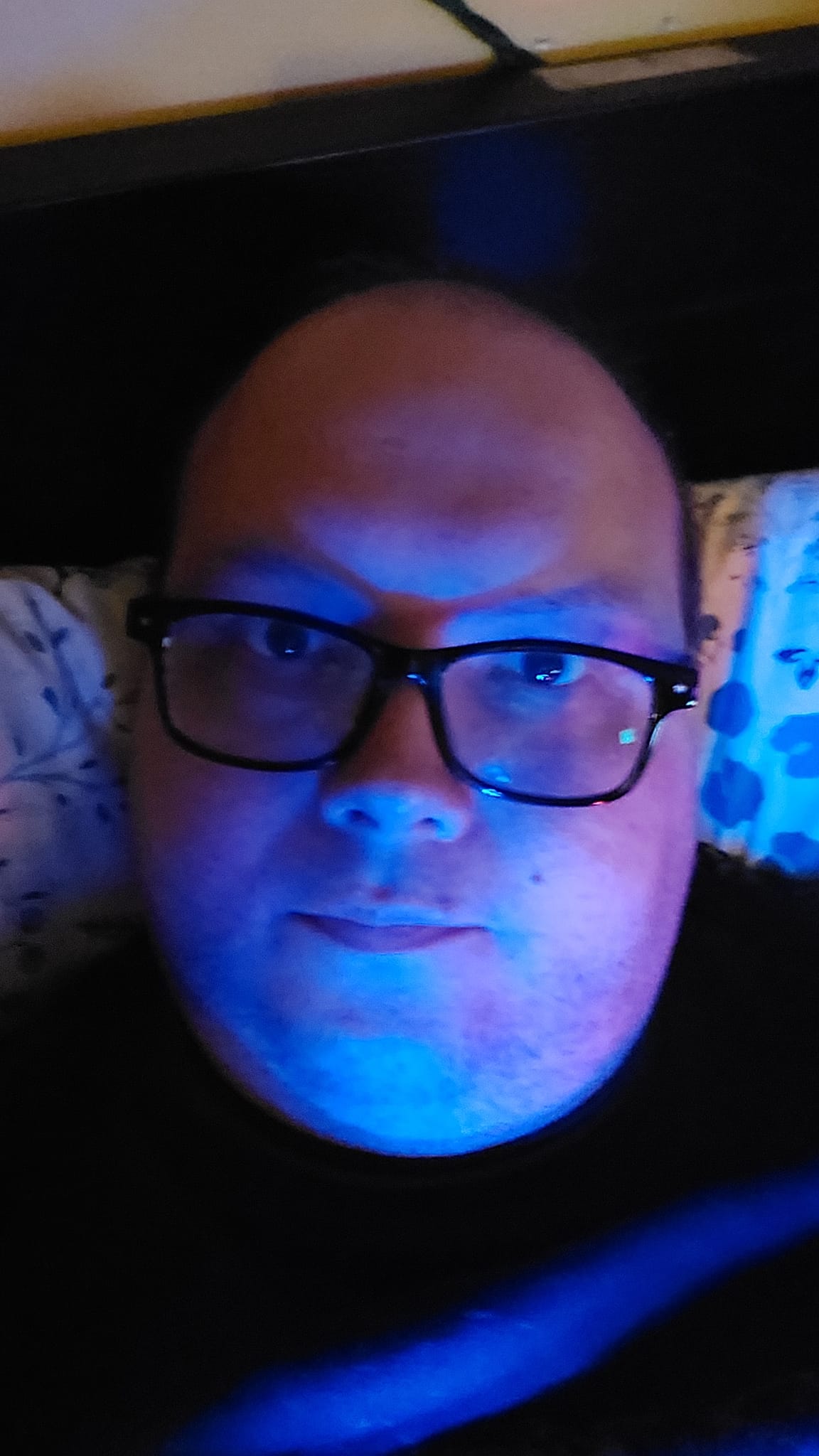 A man lays in bed, illuminated by blue light